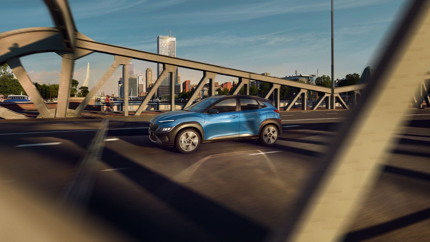 Nový Hyundai Kona ze strany v barvě  Surfy Blue, přejíždějící most.